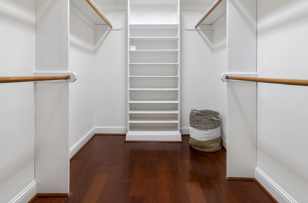 Organized walk-in closet in Lake Norman featuring white shelving, ample storage, and dark wood flooring