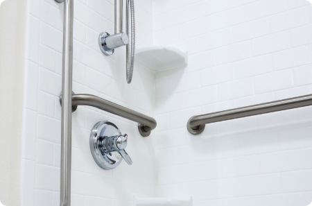 Accessible shower design featuring grab bars and a handheld showerhead in a white tiled bathroom in St. George.